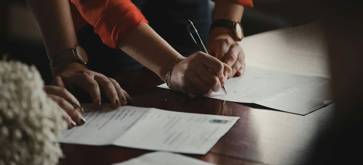 Duas pessoas a assinar documentos sobre uma mesa